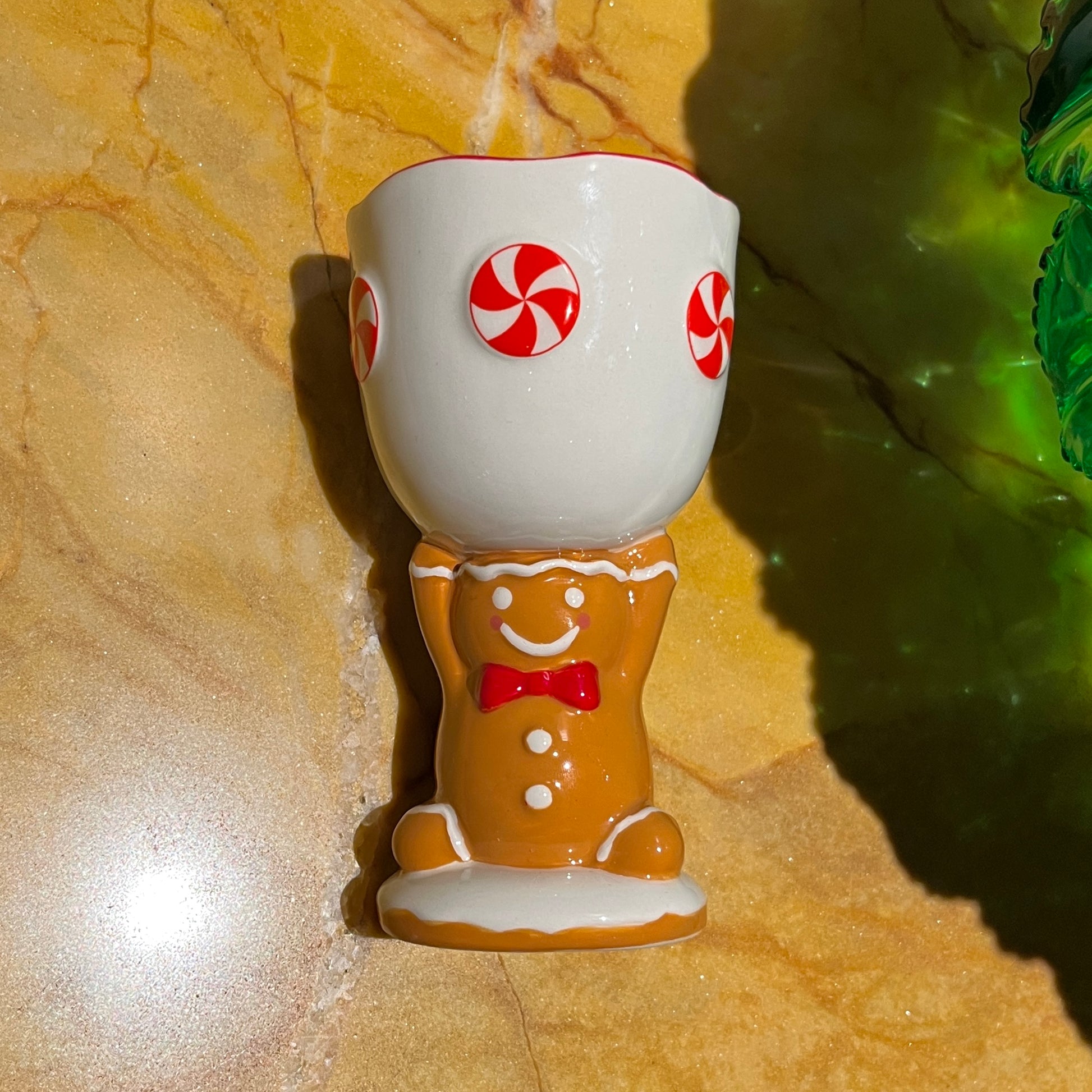 Gingerbread cookie scented ceramic gingerbread man goblet candle with peppermint candy design on a marble surface.