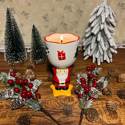 Lit spiced cranberry cider scented ceramic candle in a Santa Claus goblet, styled with pinecones, evergreen branches, and Christmas décor.
