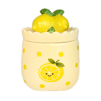 Sugared lemon zest scented candle in a cute ceramic jar with a scalloped rim, smiling lemon illustration on the front, and a lemon-shaped lid, photographed on a white background.