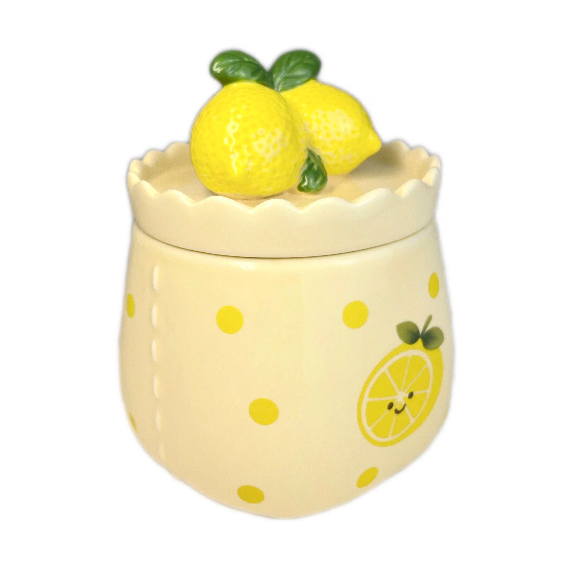 Sugared lemon zest scented candle in a cute ceramic jar with a scalloped rim, smiling lemon illustration on the front, and a lemon-shaped lid, photographed on a white background.