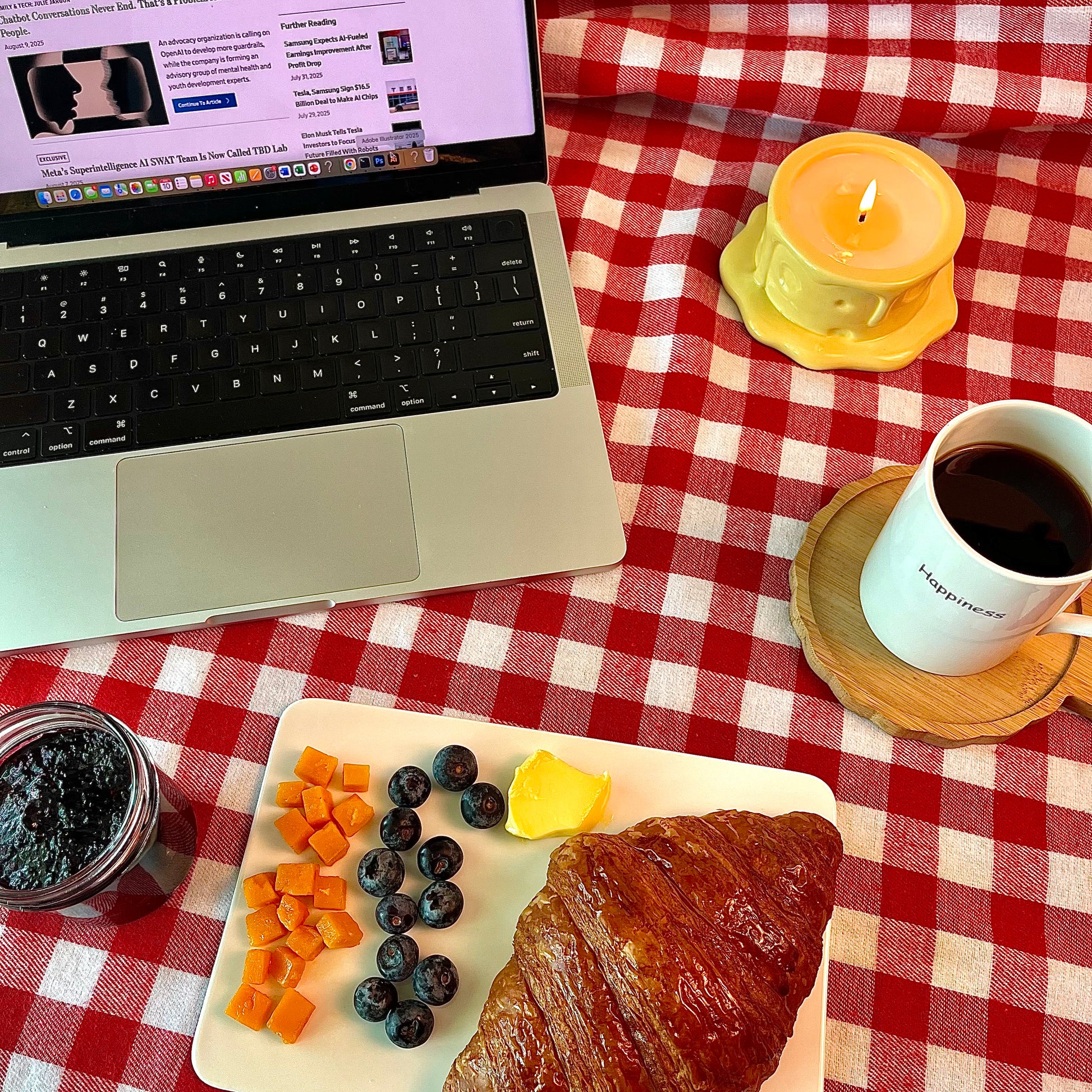 Vanilla cheesecake-scented ceramic soy candle styled on a red gingham tablecloth beside a laptop, coffee, and breakfast pastries for a cozy work-from-home scene.