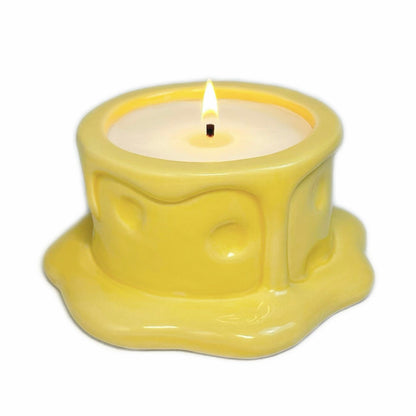 Vanilla cheesecake-scented ceramic soy candle designed like a cheese wheel with dripping glaze, photographed on a white background.