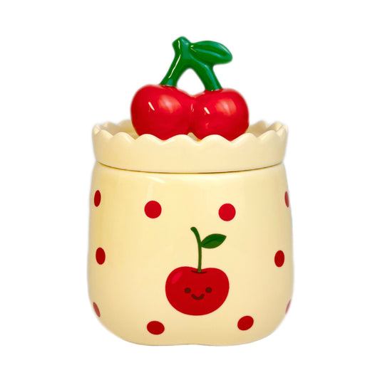 Velvet cherry scented candle in a ceramic jar with red polka dots and a smiling cherry illustration, topped with a cherry-shaped lid, photographed on a white background.